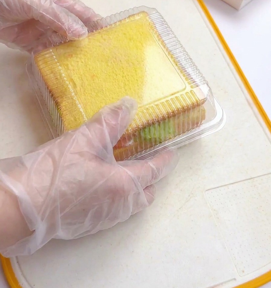 Mains pressant le couvercle dun moule transparent sur le sandwich empilé.
