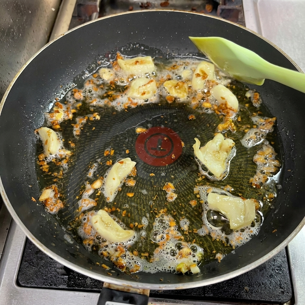 Ail haché devenant brun doré dans une poêle, remué par une spatule verte.