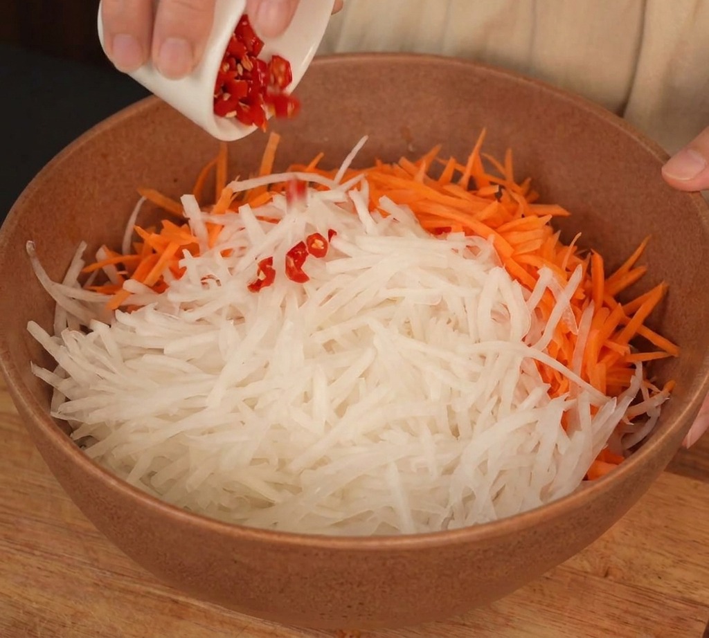 Un bol contenant du radis blanc et des carottes râpées, avec du piment rouge ajouté.