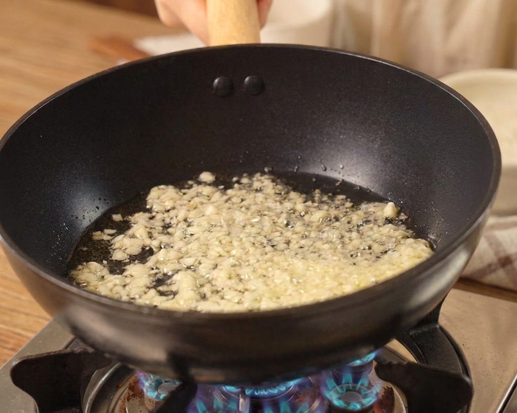 Ail haché frémissant dans de lhuile au fond dun wok noir sur une flamme de gaz bleue.
