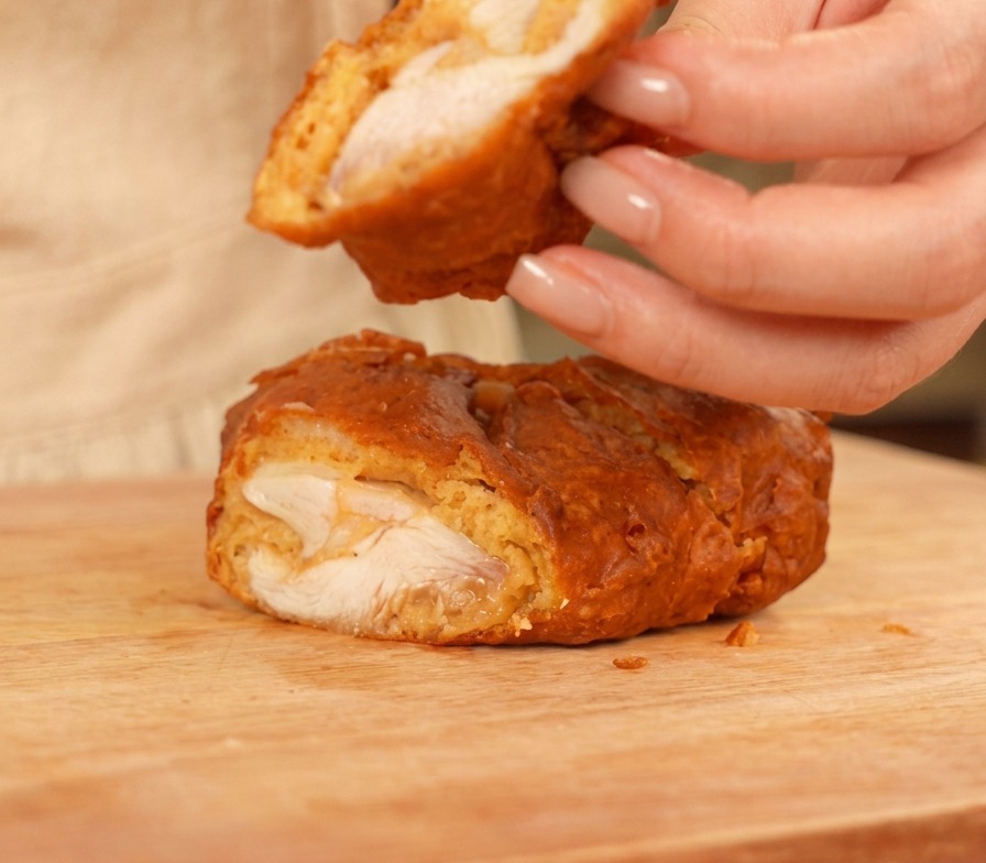 Poulet frit tranché sur une planche en bois, montrant une viande juteuse et une croûte épaisse dorée.