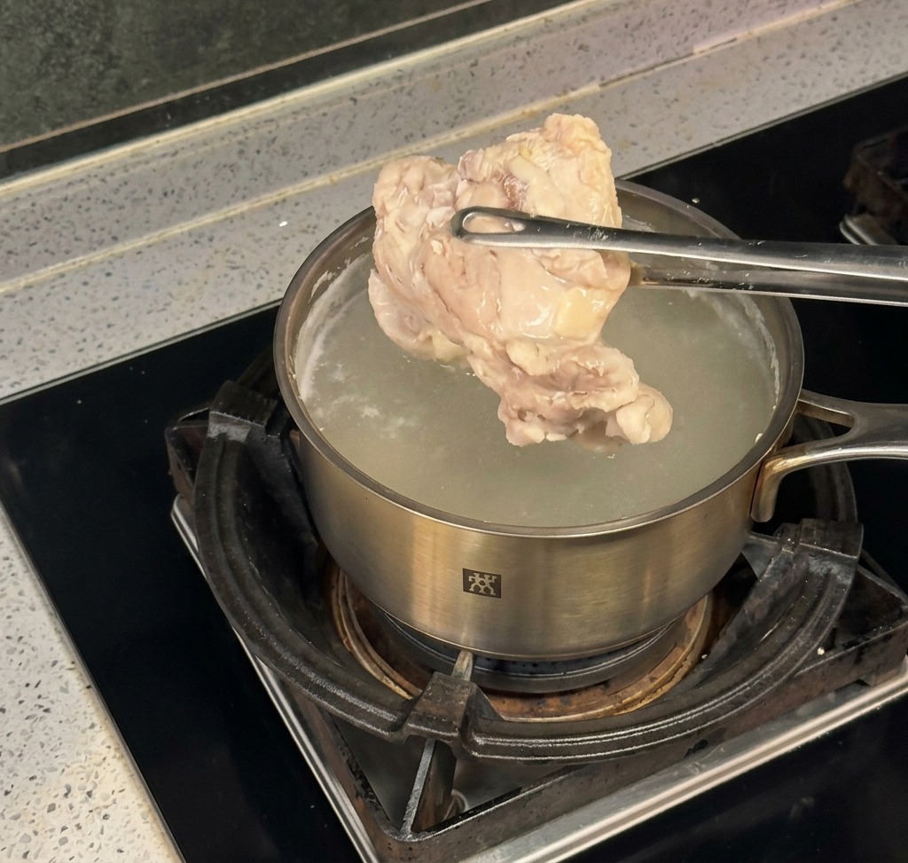 Une pince en métal sortant un morceau de poulet poché dune casserole deau bouillante sur une cuisinière.
