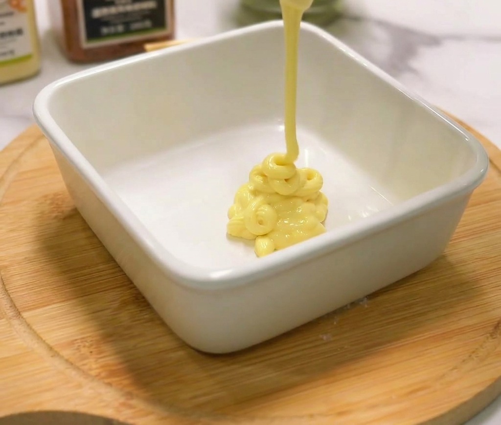 Mayonnaise crémeuse versée dune bouteille dans un petit bol en céramique sur une planche en bois.