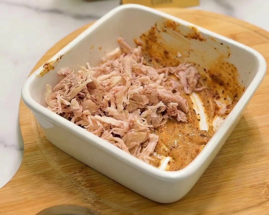 Le poulet effiloché ajouté à la sauce crémeuse orange dans un bol carré blanc.