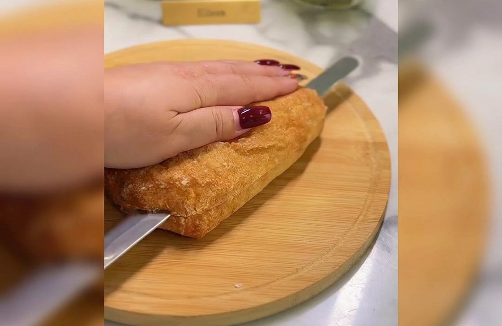 Une main tenant une ciabatta tandis quun couteau à pain scie le pain horizontalement sur une planche en bois.