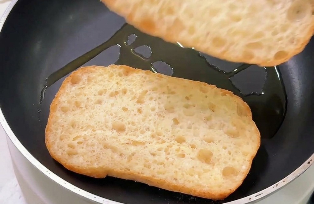 Deux morceaux de pain ciabatta grillant face coupée vers le bas dans une poêle légèrement huilée.