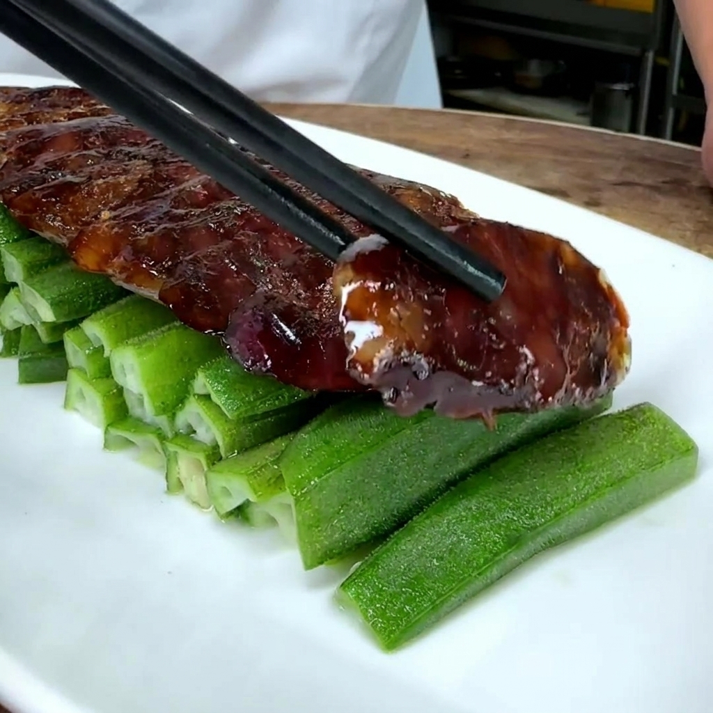 Gros plan de rondelles de saucisse chinoise déposées sur un lit de gombo vert dans une assiette blanche.