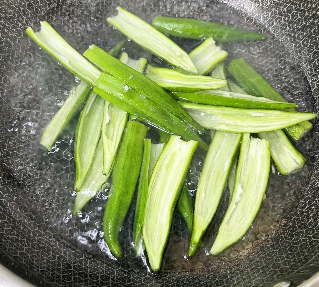 Coques de gombo fendues en train de bouillir dans une casserole deau sur la cuisinière.