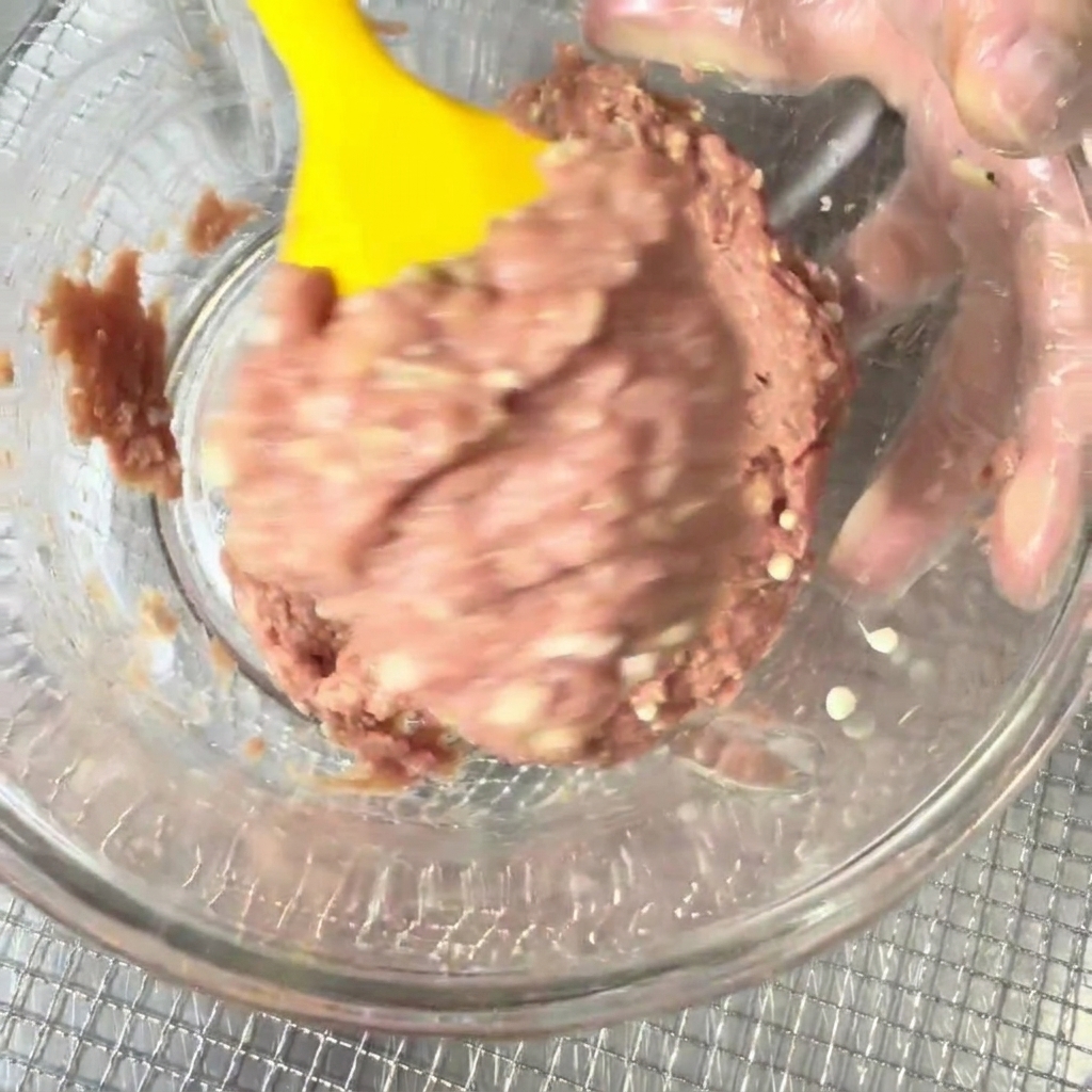 Viande de canard hachée et graines dokra combinées dans un bol avec une spatule en silicone jaune.