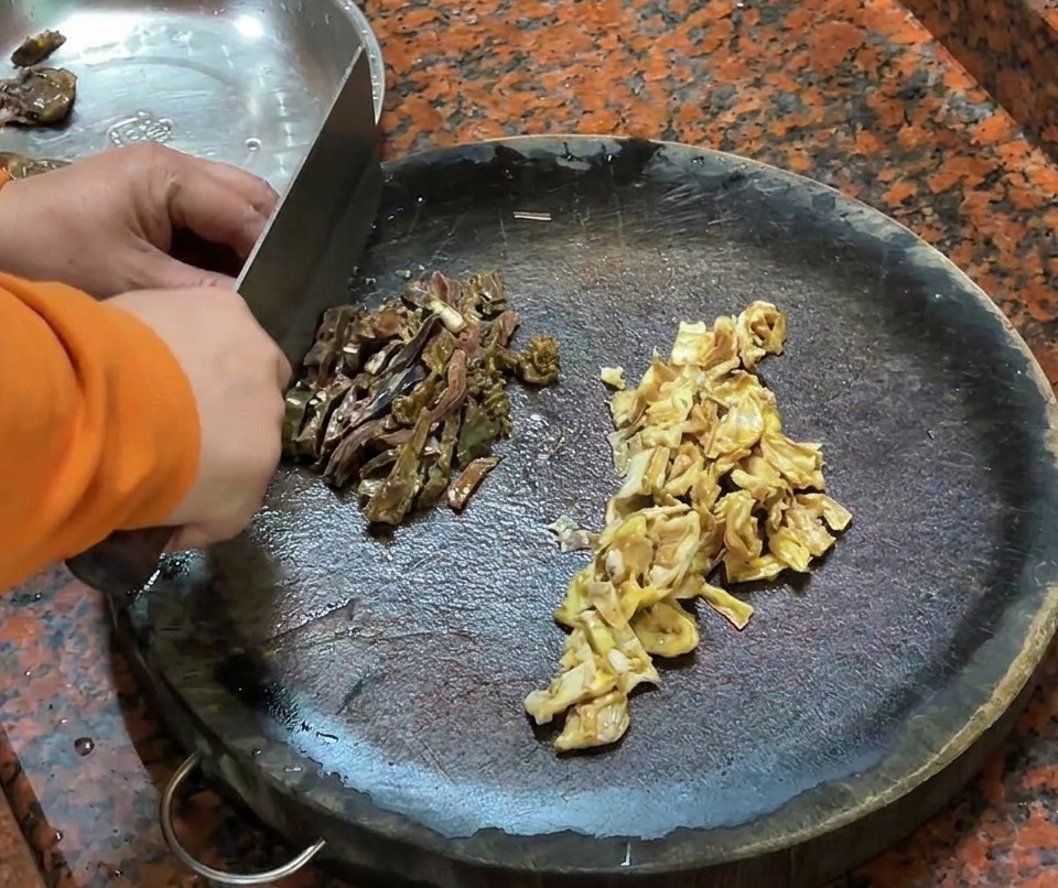Saucisse de foie de canard et morceaux de peau de canard découpés sur une planche à découper en bois.