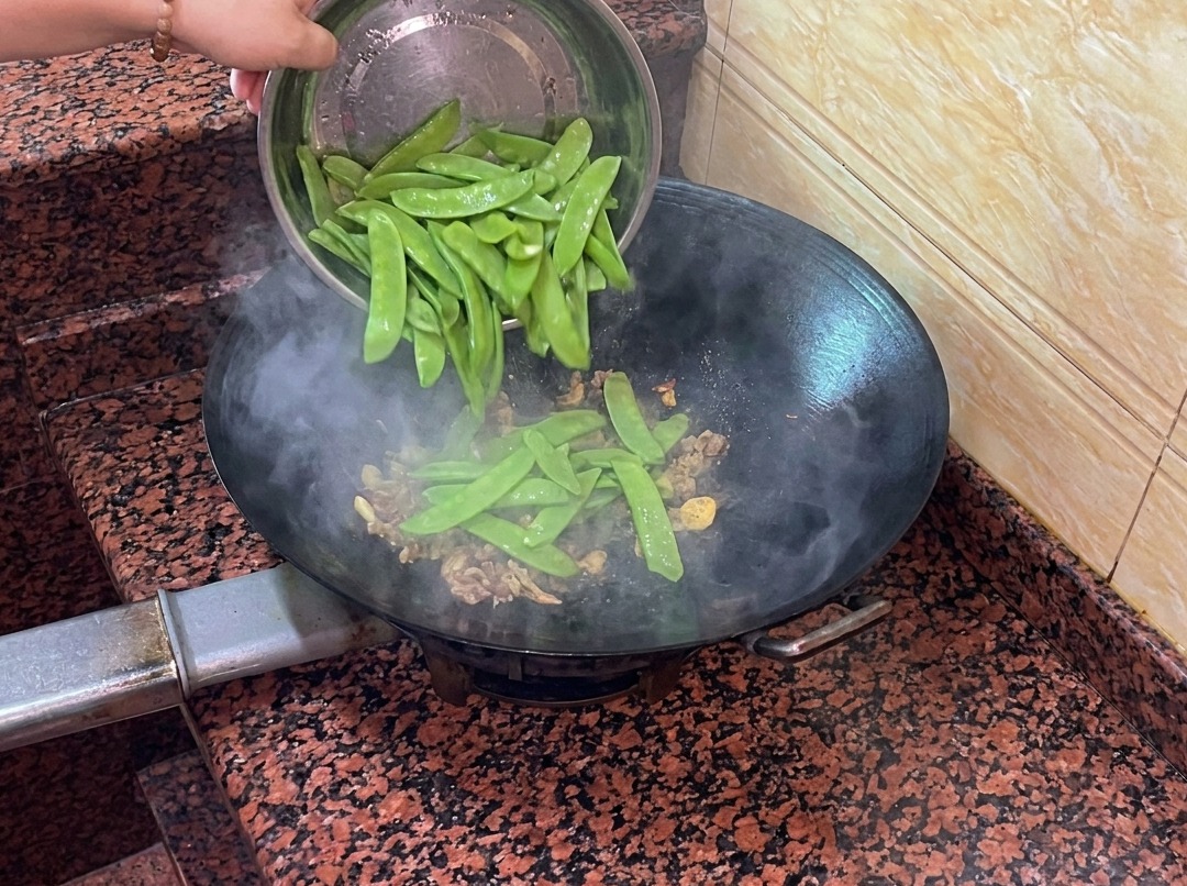 Pois gourmands frais ajoutés dans le wok avec la saucisse et les aromates.