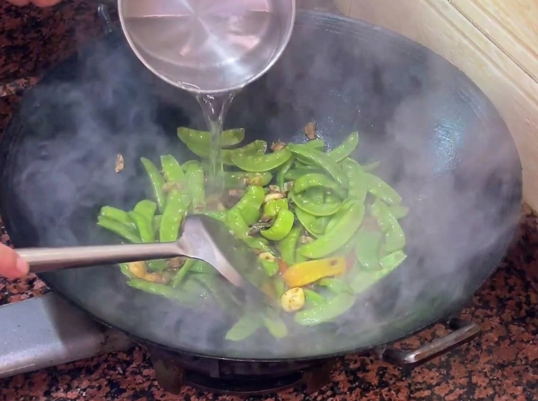 Eau tiède versée dans le wok avec les pois gourmands et la saucisse.