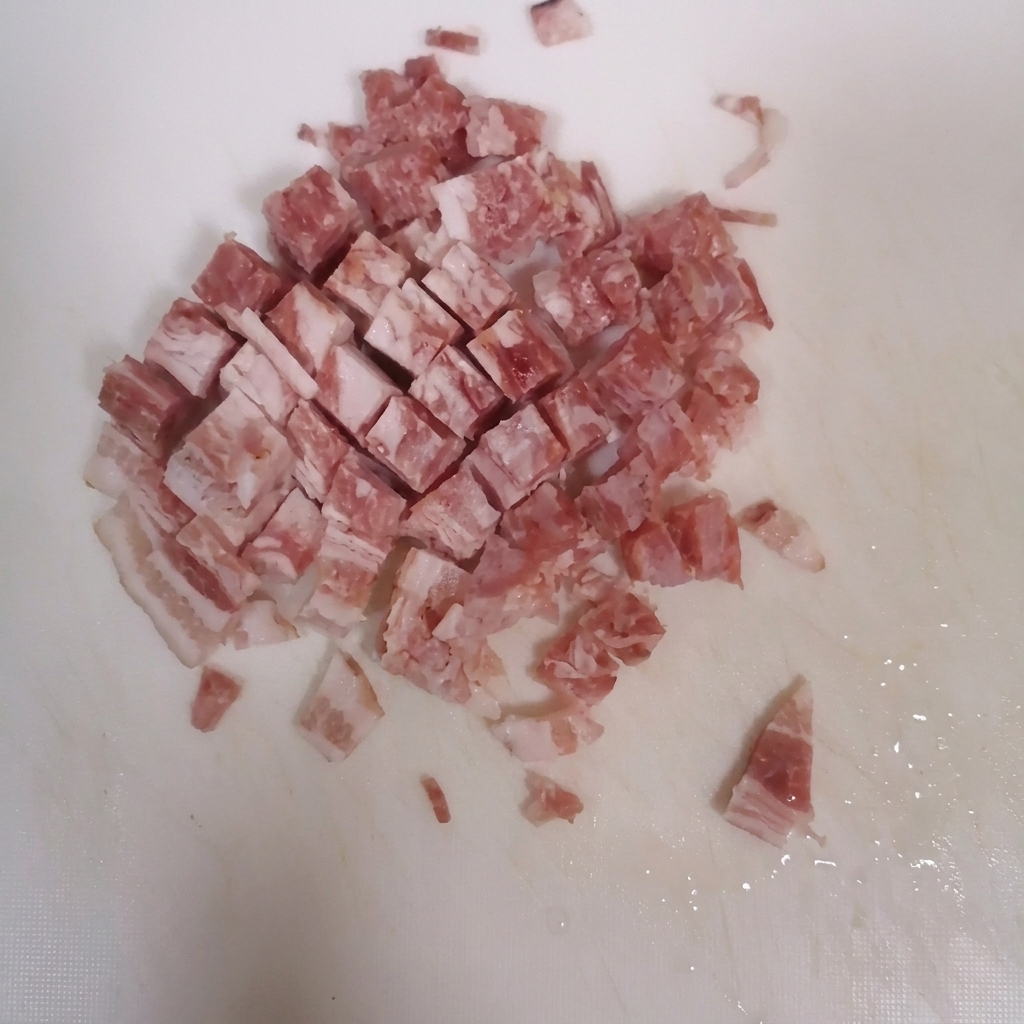 Tranches de lard coupées en petits dés sur une planche à découper blanche.