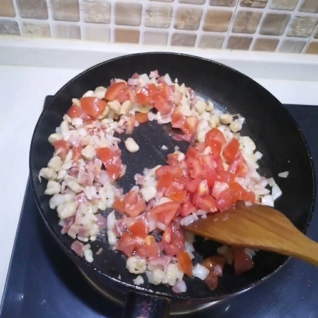 Des dés de tomates ajoutés dans une poêle contenant la viande et les oignons rissolés.