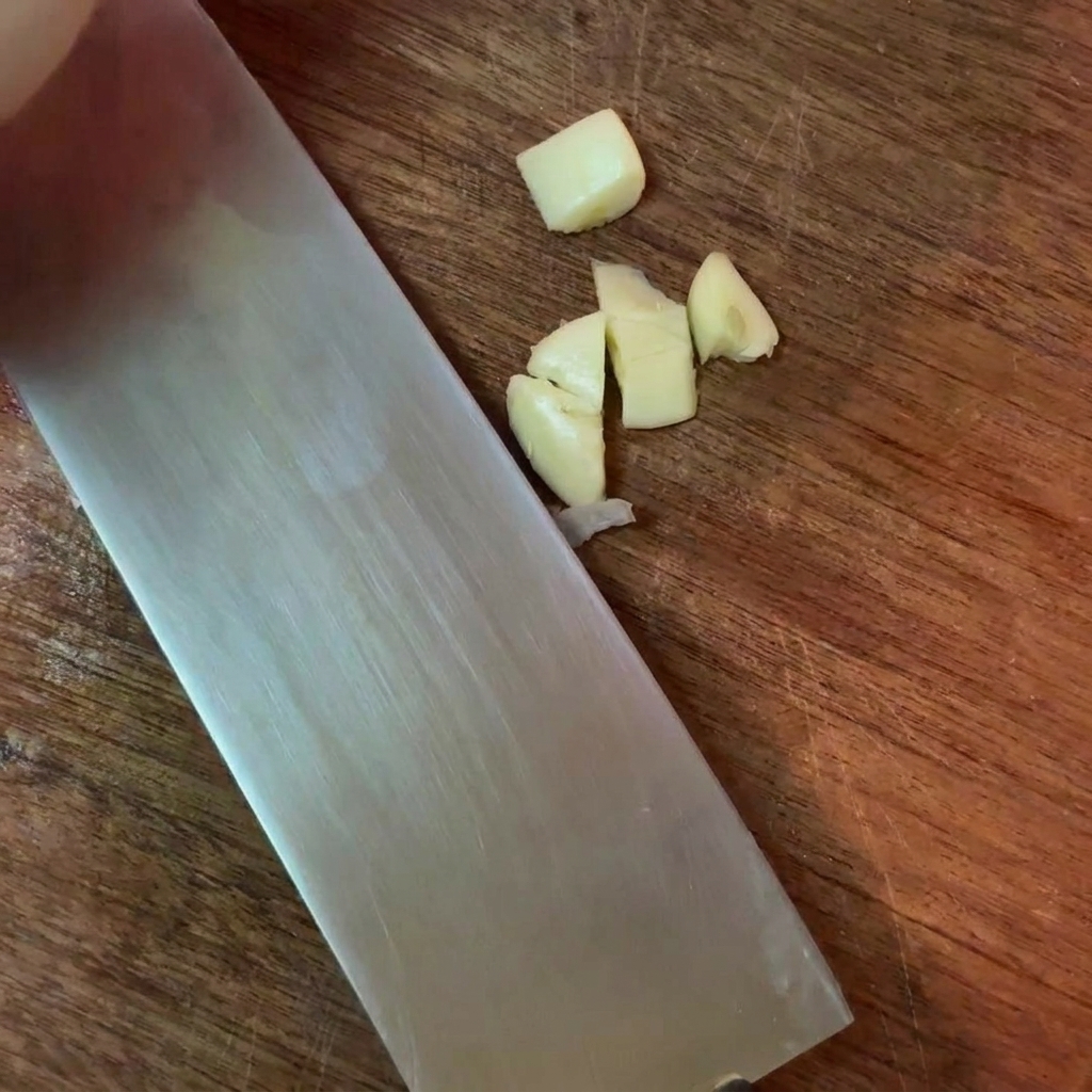 Gousses dail grossièrement hachées à côté dun grand couteau en métal sur une surface en bois.