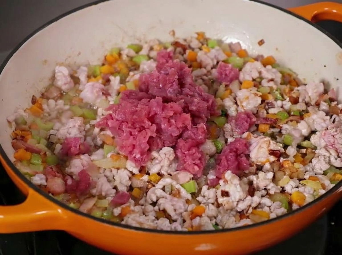 Bœuf et porc hachés en train de cuire avec des légumes en dés dans une grande poêle en fonte émaillée.