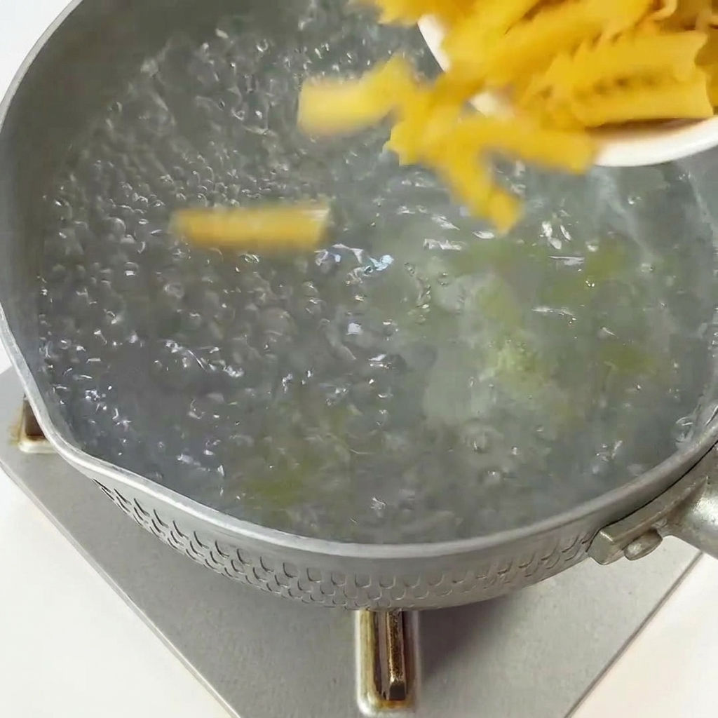 Fusillis secs versés dun petit plat dans une casserole deau bouillante.