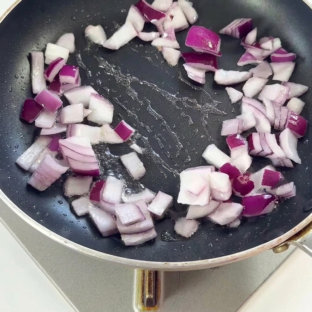 Morceaux de bacon et oignons rouges sautés ensemble dans une poêle noire.