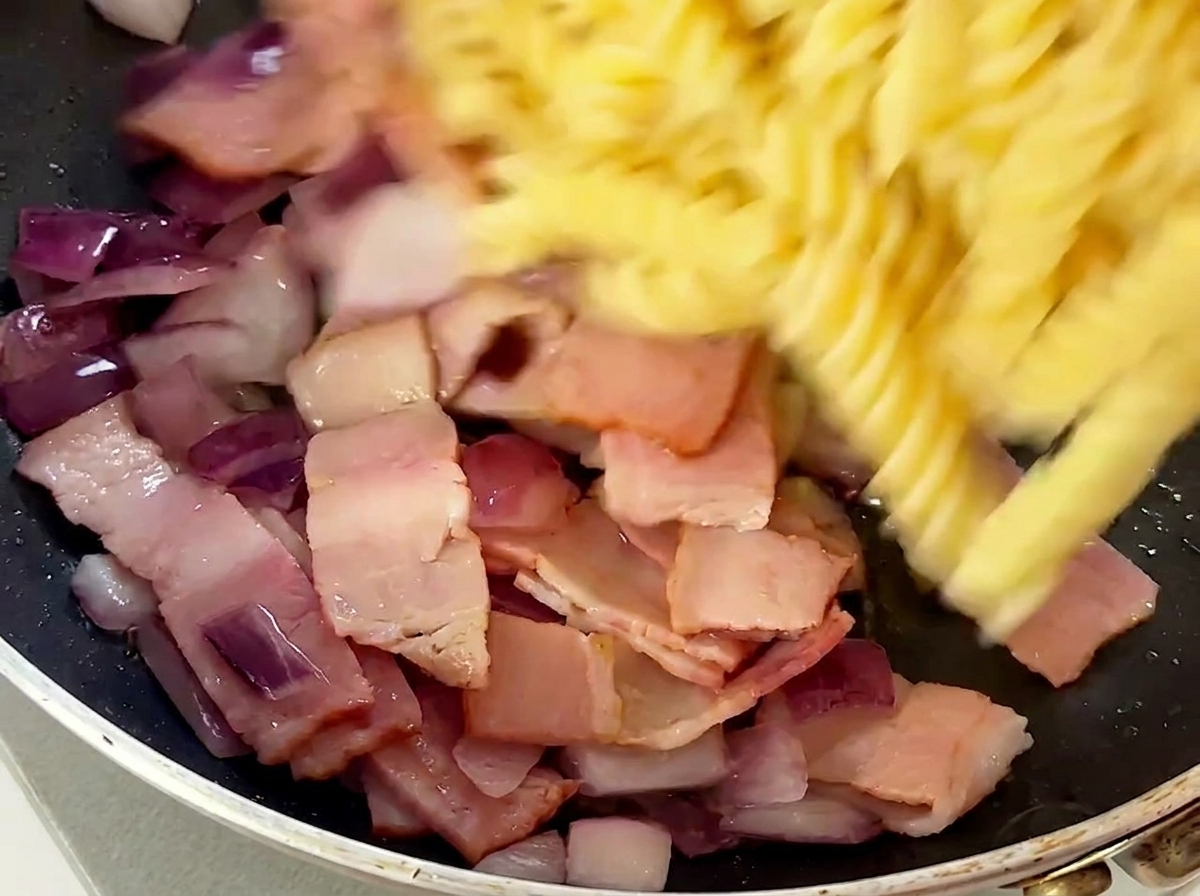 Fusillis cuits ajoutés dans la poêle contenant le bacon et les oignons.