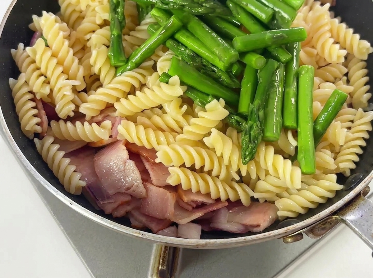 Asperges et assaisonnements mélangés avec des pâtes, du bacon et des oignons dans une poêle.