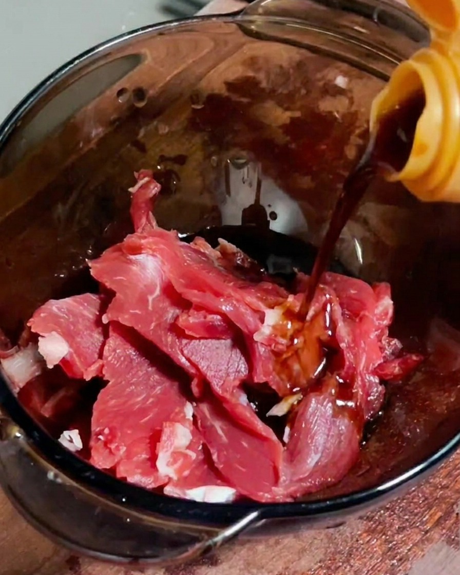 Sauce soja versée sur des tranches de bœuf cru dans un bol transparent.