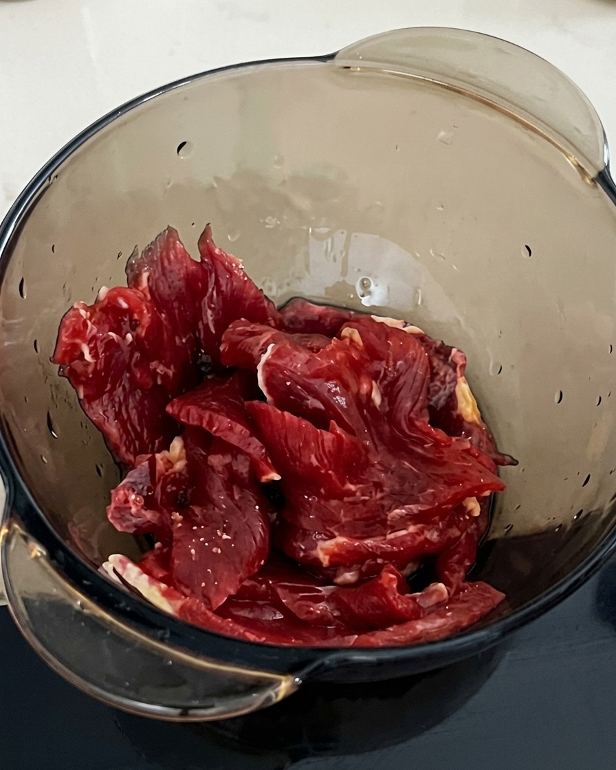 Une cuillerée de fécule ajoutée au bol contenant le bœuf et la sauce soja.