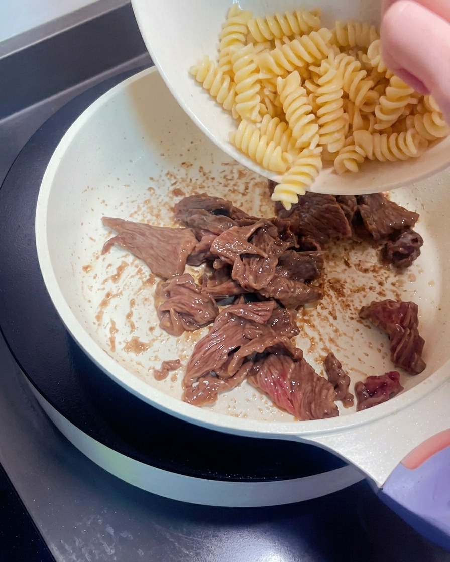 Pâtes en spirale transférées dans une poêle contenant le bœuf cuit.