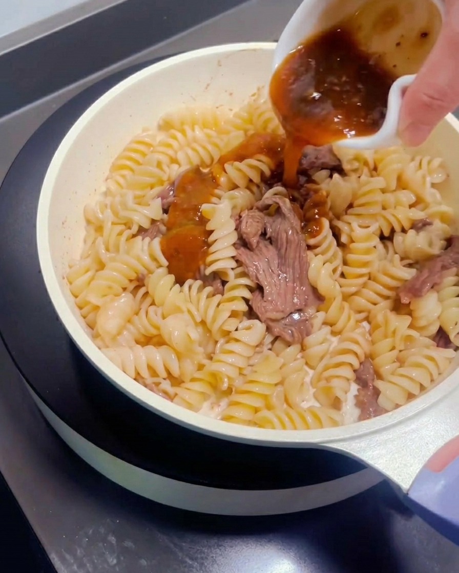 Sauce pour pâtes versée sur le mélange de bœuf et de pâtes.