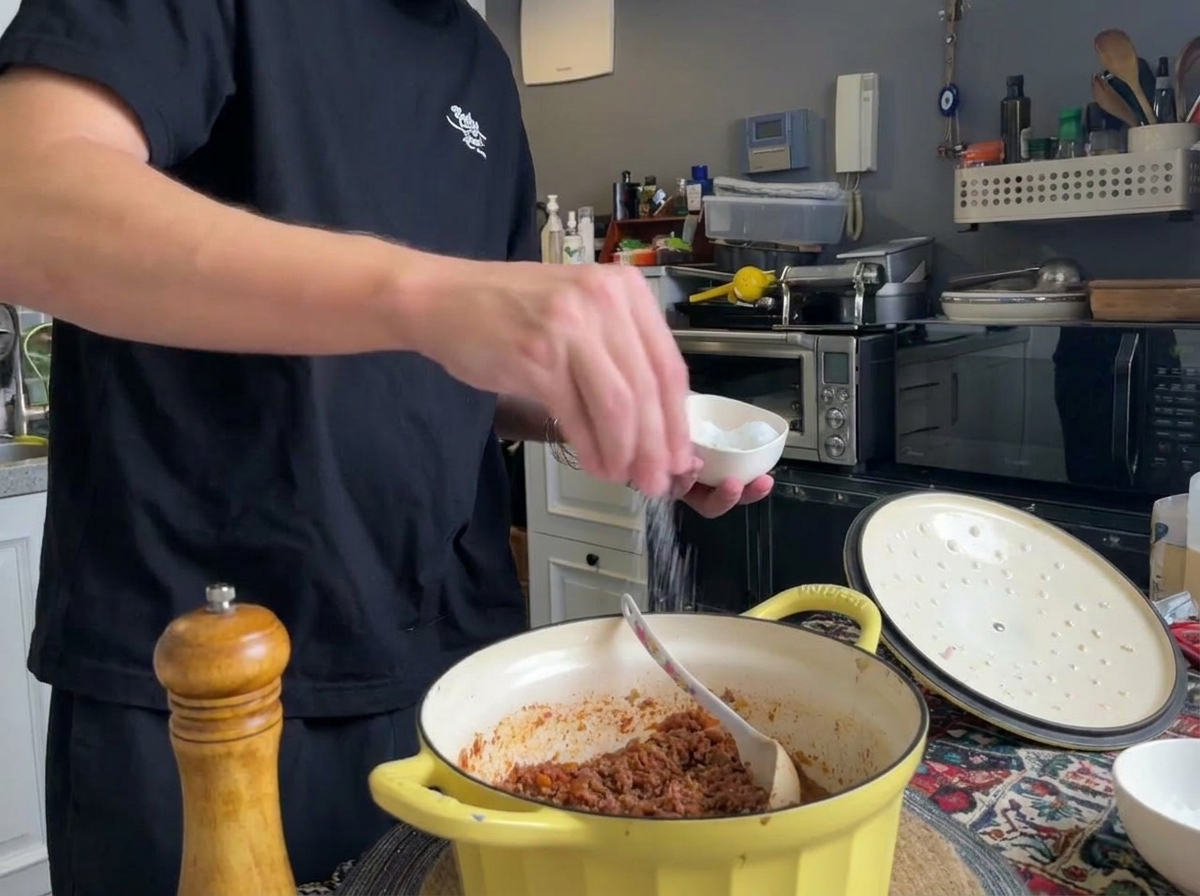 Poivre noir fraîchement moulu et sel ajoutés dans une casserole de ragù de viande terminé.