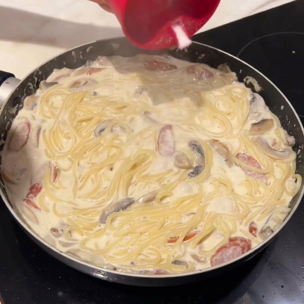 Spaghettis cuits ajoutés à la sauce crémeuse dans la poêle.