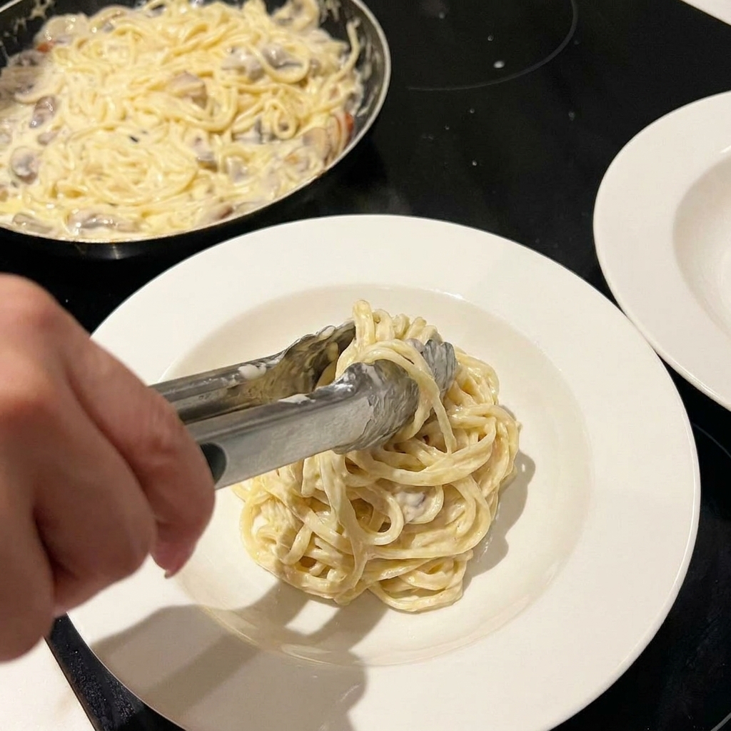 Pâtes crémeuses mélangées dans une poêle, saupoudrées de fromage et dherbes.
