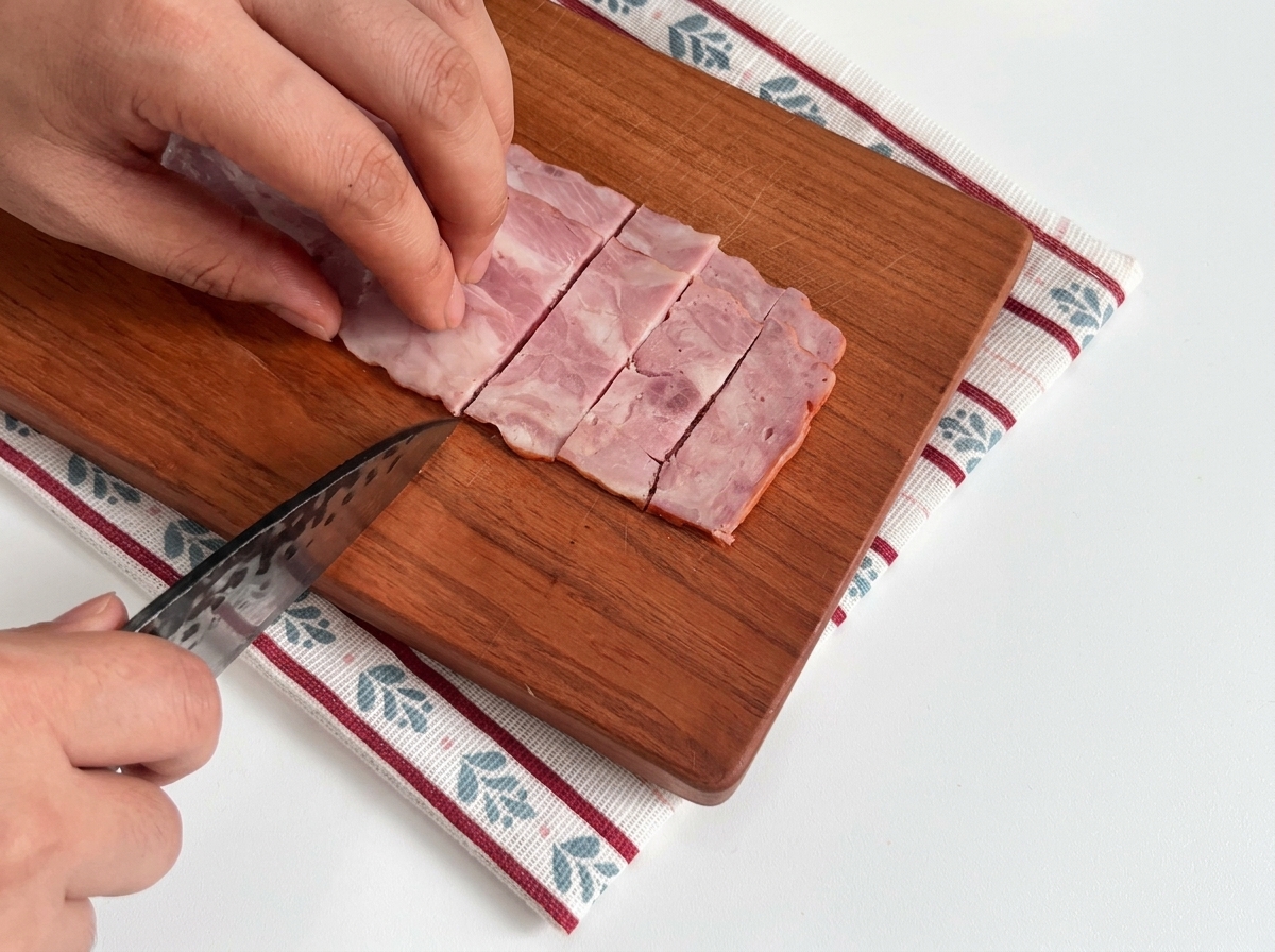 Tranches de lardons crus soigneusement disposées sur une planche en bois prêtes à être cuisinées.