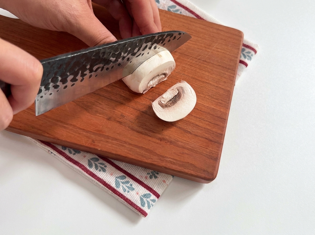 Champignons de Paris frais en cours de découpe sur une planche en bois.