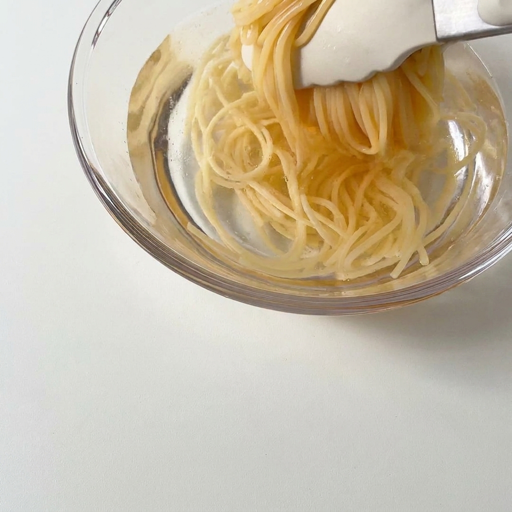 Spaghettis cuits soulevés avec des pinces et placés dans un bol deau froide.