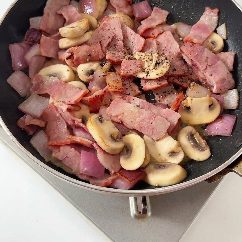 Poivre noir fraîchement moulu ajouté sur le mélange de lardons et champignons sautés.