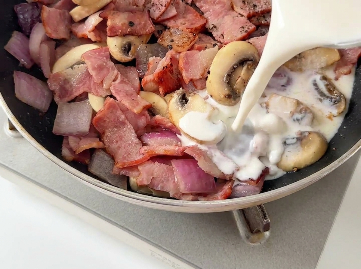 Lait et crème liquide versés dun verre mesureur dans une poêle contenant des lardons et champignons.
