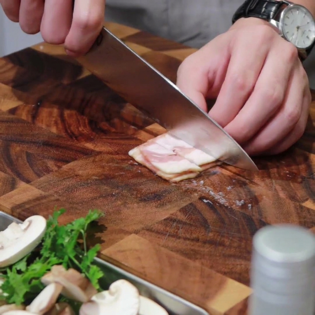 Tranches de bacon coupées en morceaux sur une planche à découper en bois.