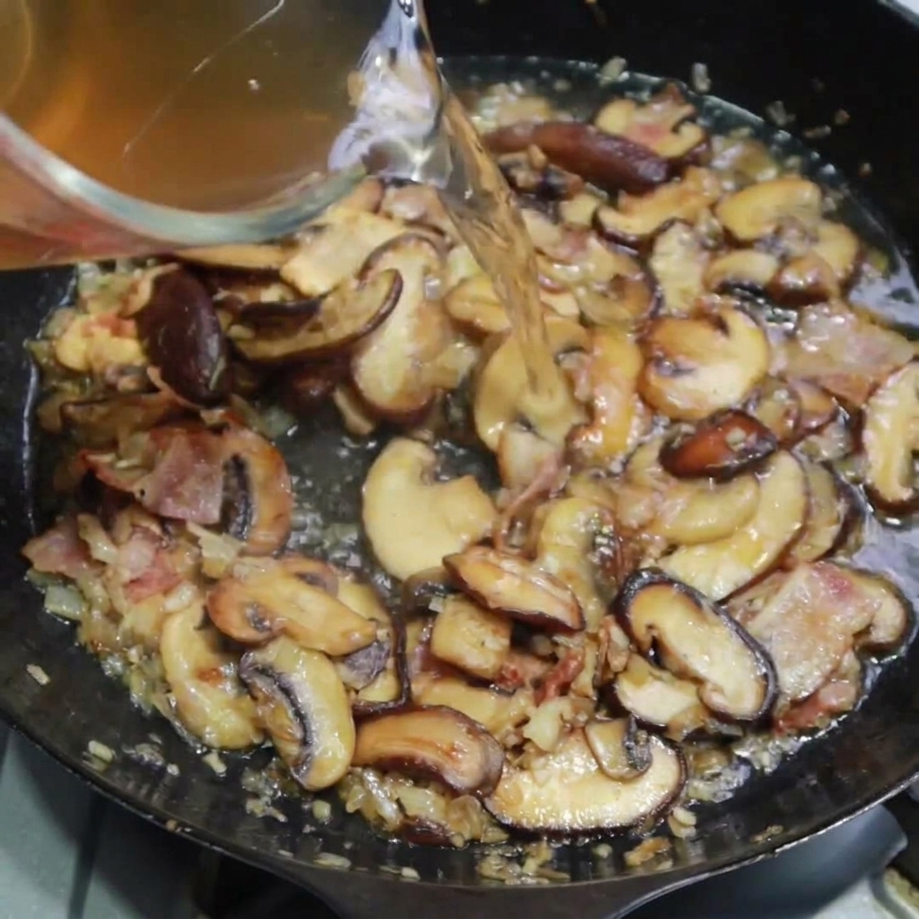 Bouillon de volaille versé dans la poêle avec le mélange de bacon et champignons.
