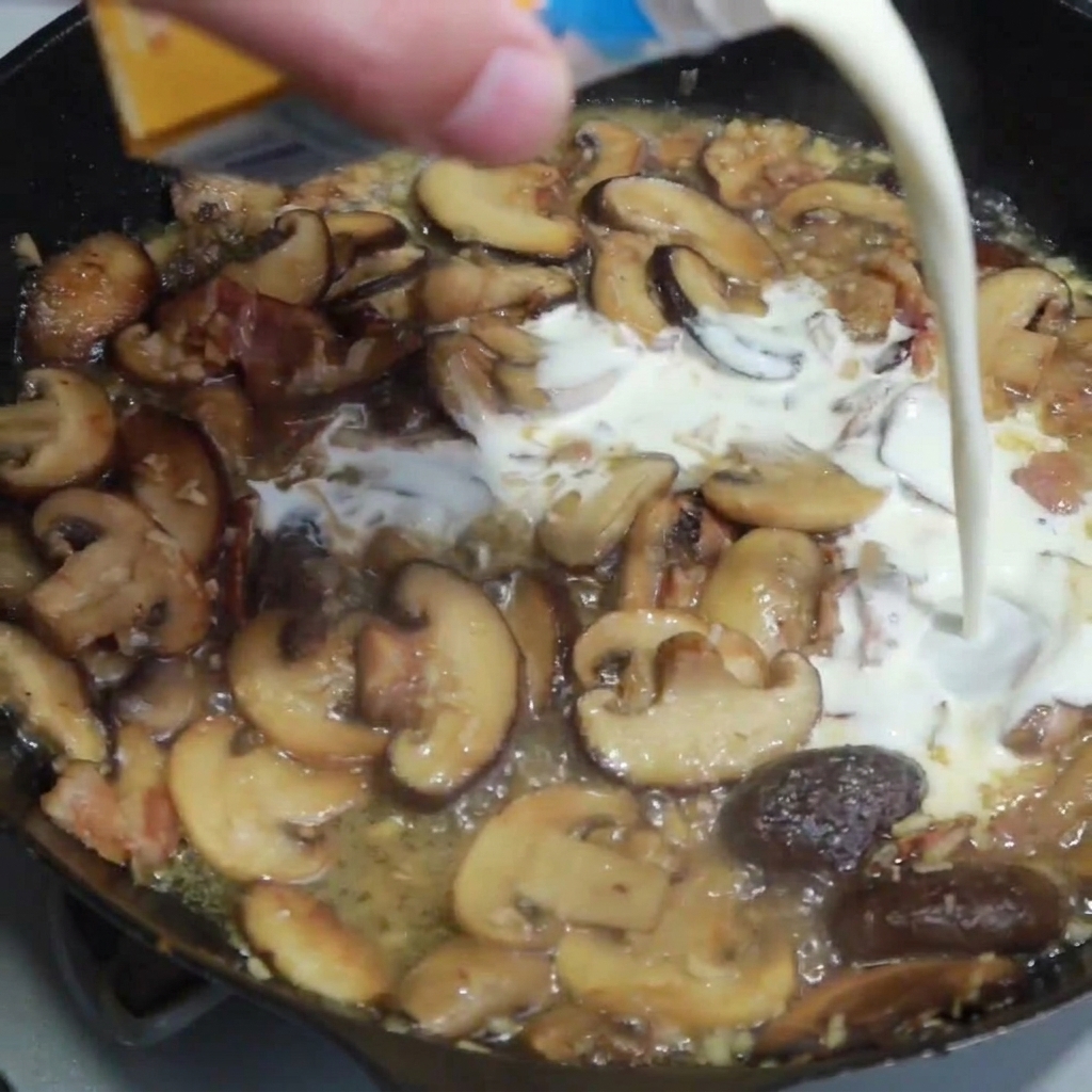 Crème liquide versée dans la poêle avec les champignons, le bacon et les oignons dorés.