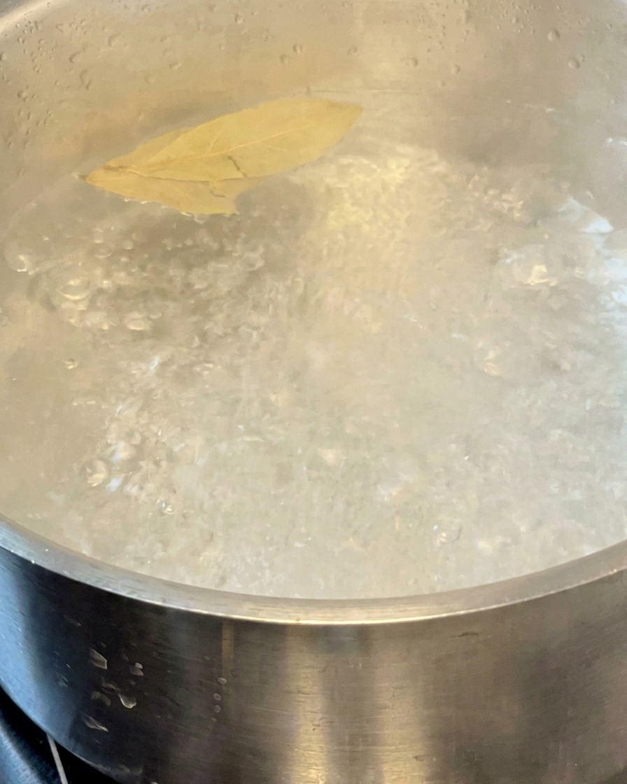Pâtes en train de cuire dans une casserole deau bouillante avec deux feuilles de laurier.