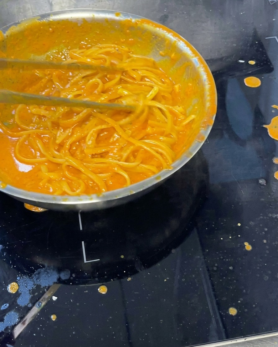 Pâtes crémeuses mélangées à la sauce poivron, avec une louche pour remuer.