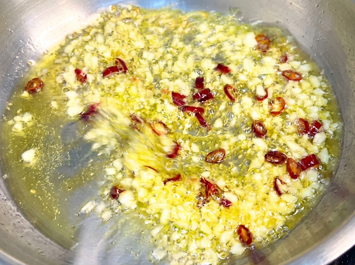 Pâtes mélangées dans une poêle avec de lail doré et des flocons de piment, enrobées dune sauce brillante.