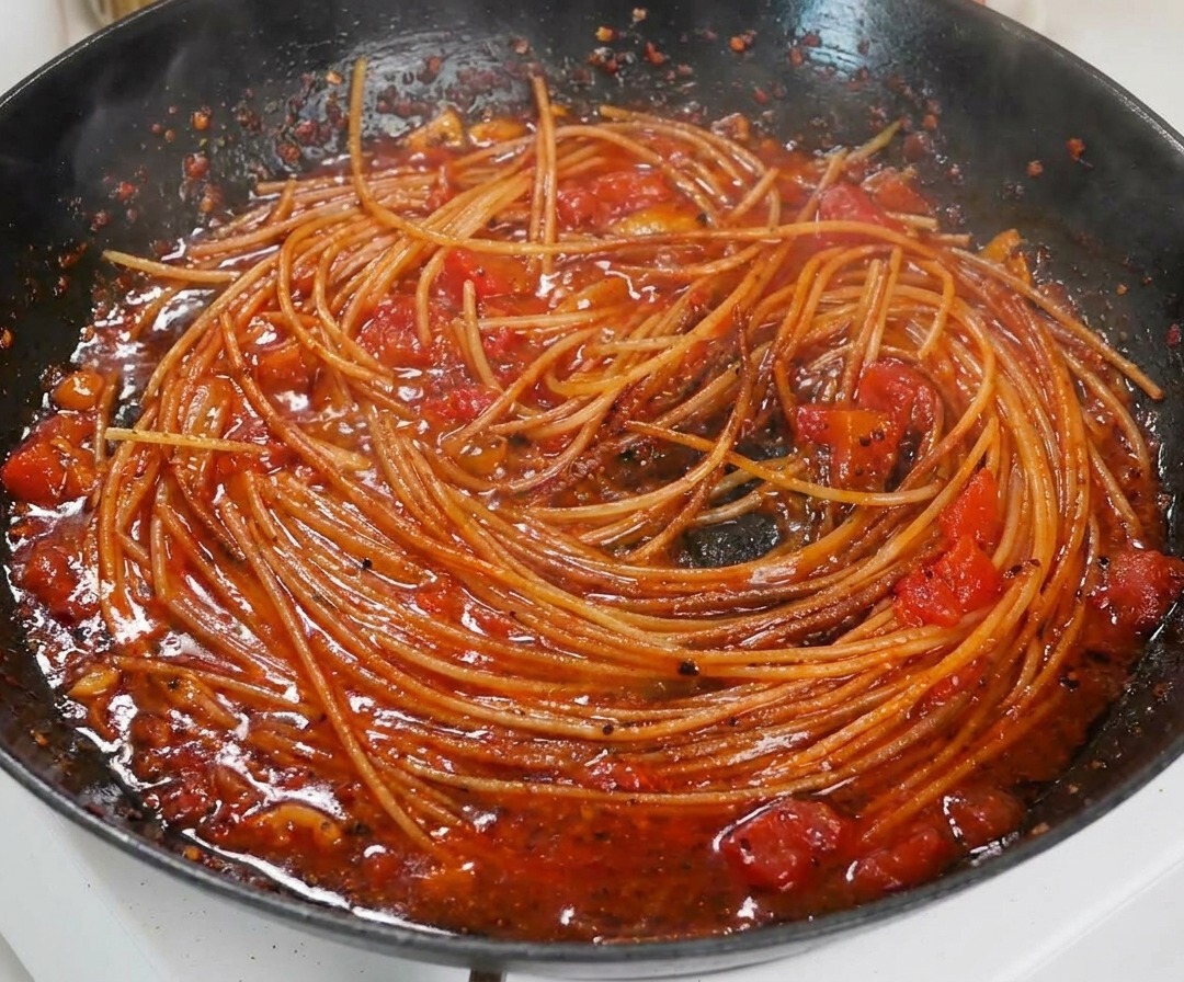 Gros plan sur des spaghetti cuits et enrobés dune sauce tomate épaisse et onctueuse dans une poêle.