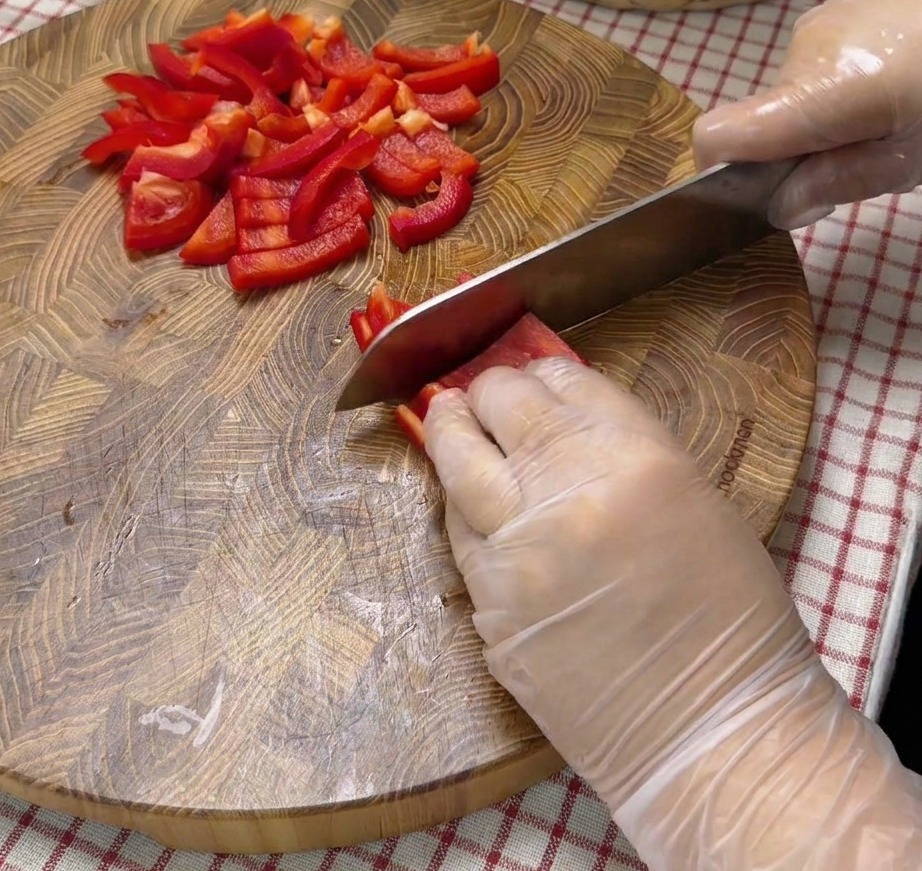 Dés de poivrons rouges disposés sur une planche à découper en bois.