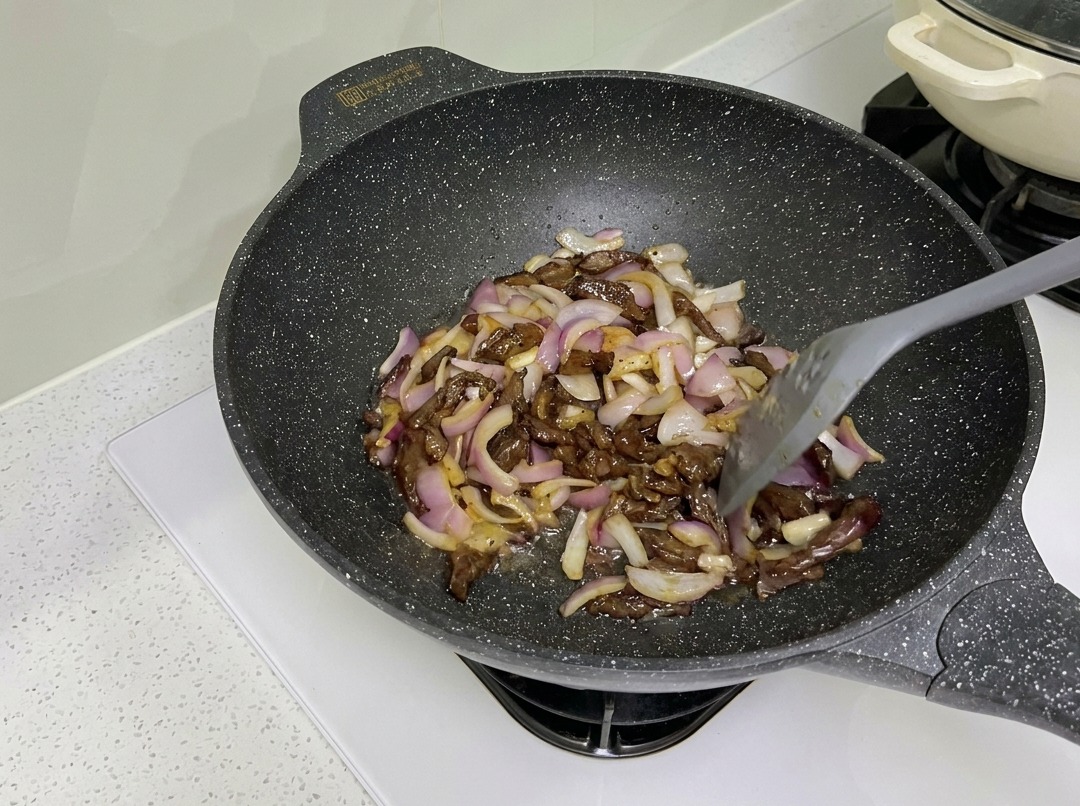 Lanières de bœuf et oignons rouges sautés ensemble dans un wok.