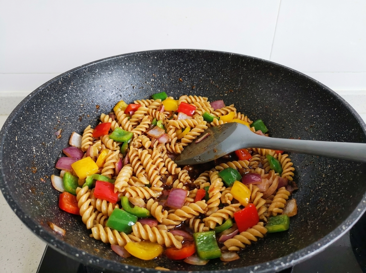 Rotinis, bœuf et poivrons sautés à la spatule dans un wok, bien enrobés de sauce.