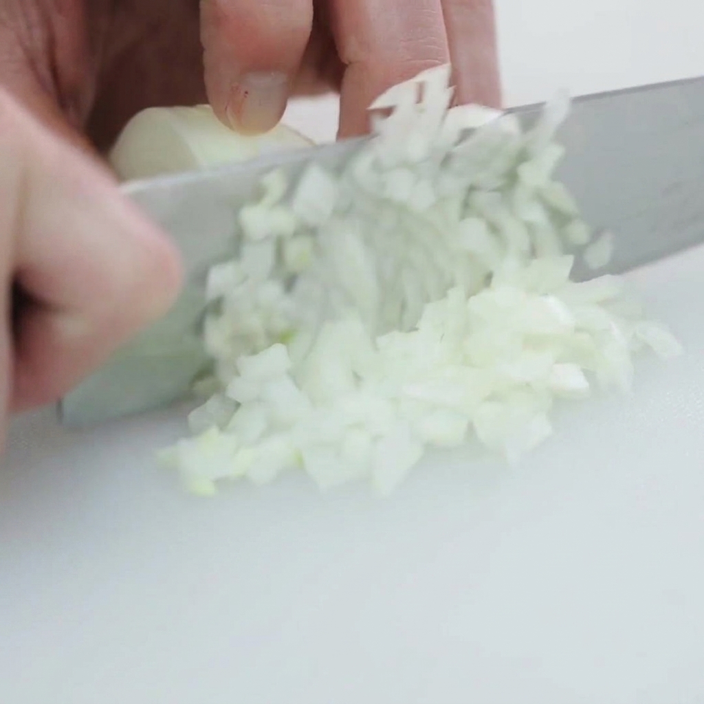 Un oignon blanc coupé en petits morceaux réguliers sur une planche à découper blanche.