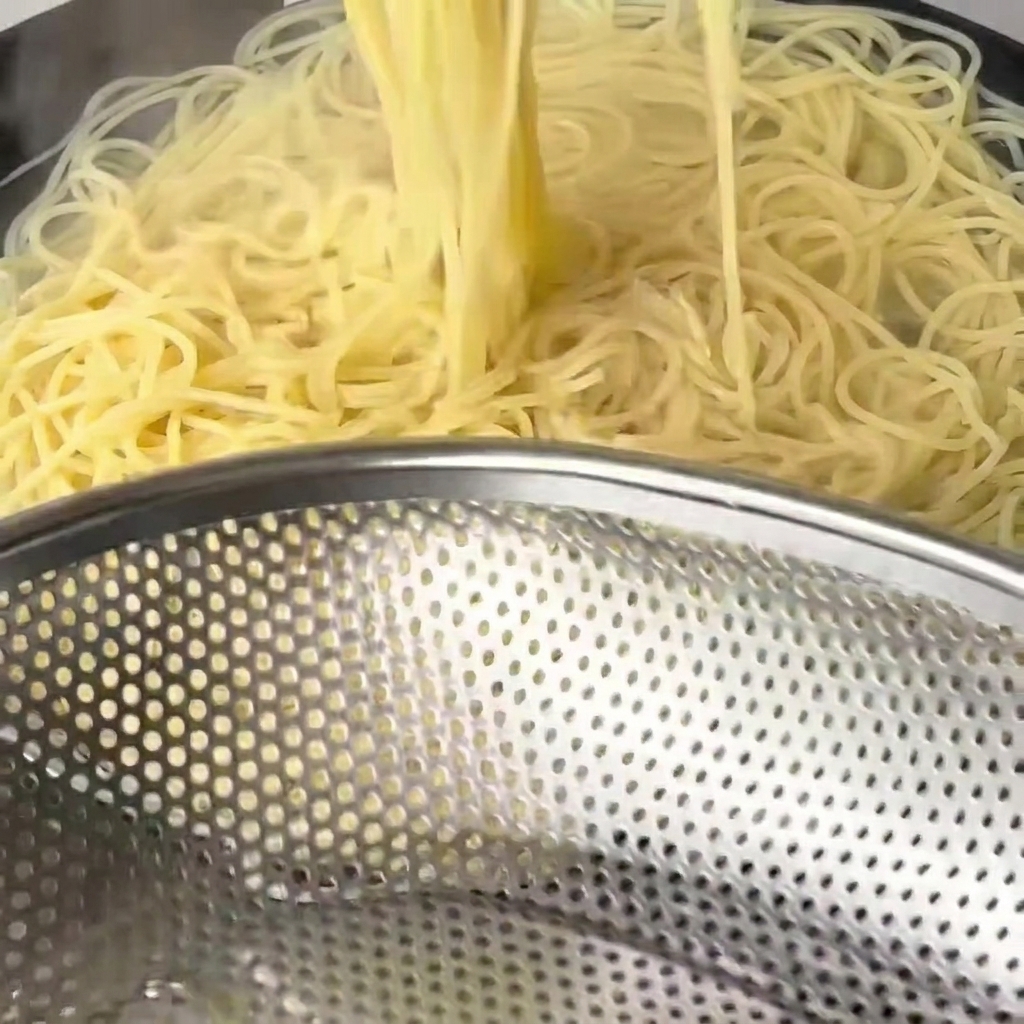 Les spaghetti cuits sont retirés de leau avec de grandes baguettes en bois.