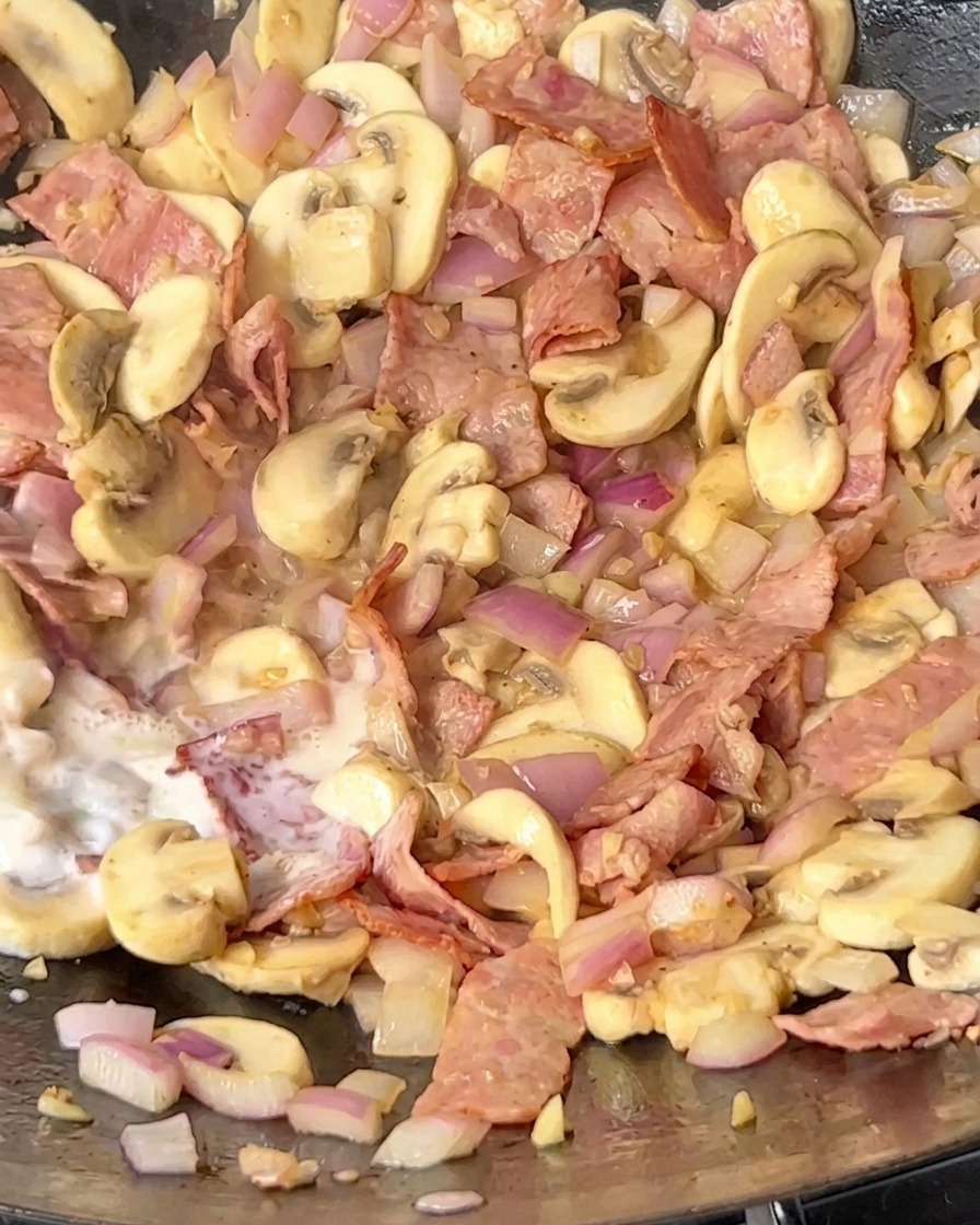 Lait versé dans le wok sur le mélange bacon, champignons et oignons.