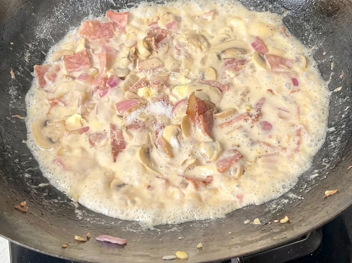Spaghetti cuits ajoutés dans le wok contenant la sauce crémeuse.